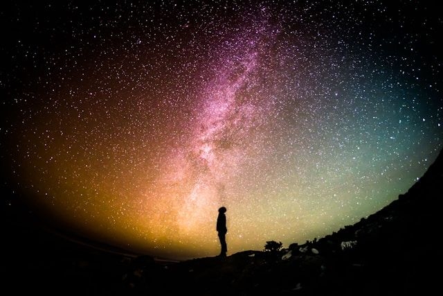 Photo by Greg Rakozy on Unsplash of a sillhouette standing beneath a starry sky